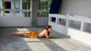 Junge Frau in gelber Hose übt Yin Yoga Position Krokodil